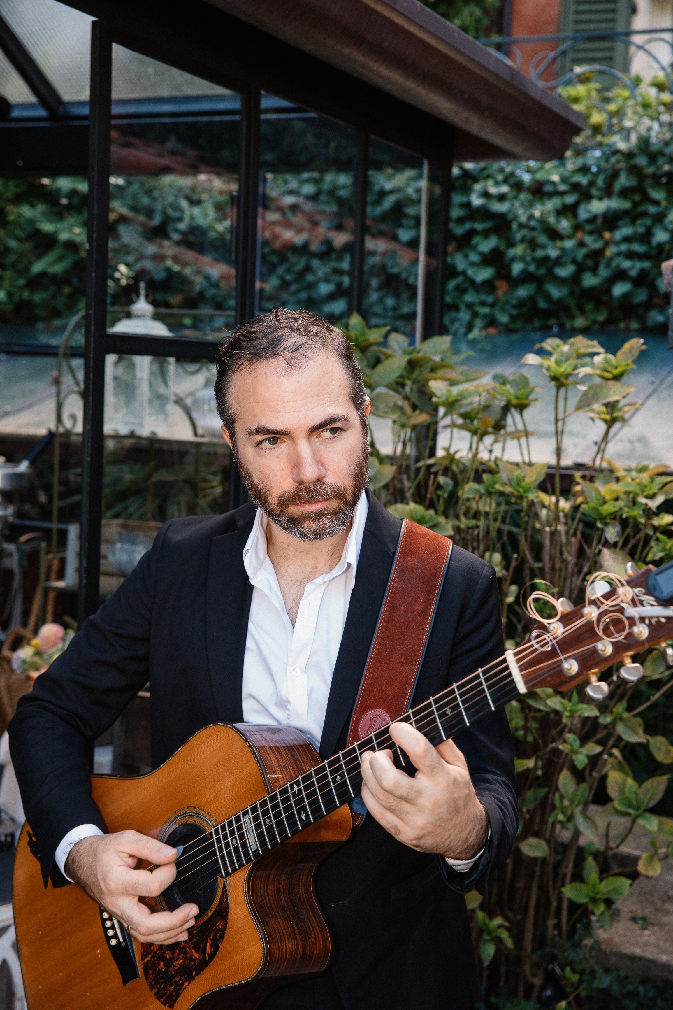 Guitarist performing live acoustic music at a small wedding in Italy surrounded by lush garden greenery and elegant venue decor.