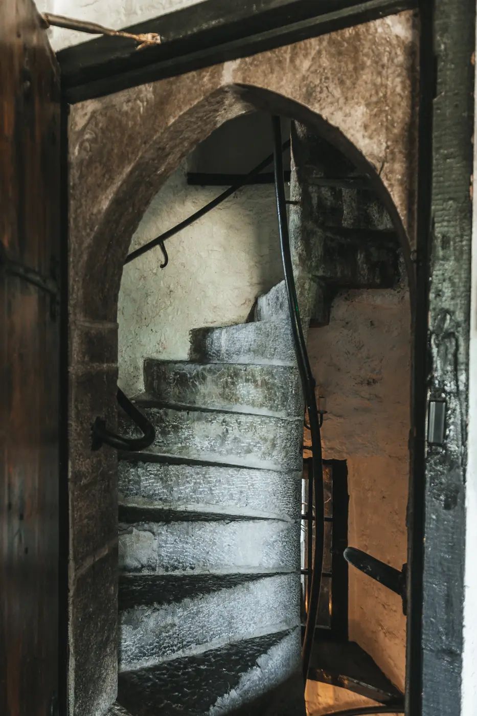 Worn stone spiral staircase climbing the medieval tower behind a pointed-arch doorway.