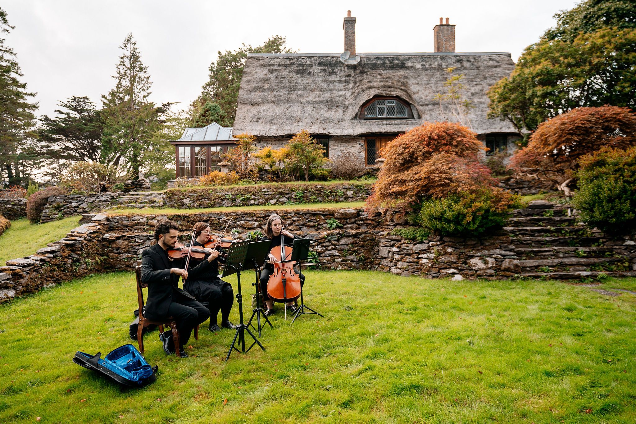 Three musicians playing stringed instruments with autumn nature behind them during a ceremony of an elopement in Ireland