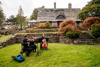 Three musicians playing stringed instruments with autumn nature behind them during a ceremony of an elopement in Ireland