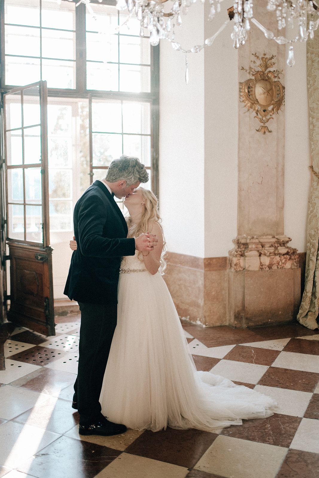 Couple dancing beneath a crystal chandelier in a marble palace hall in Austria
