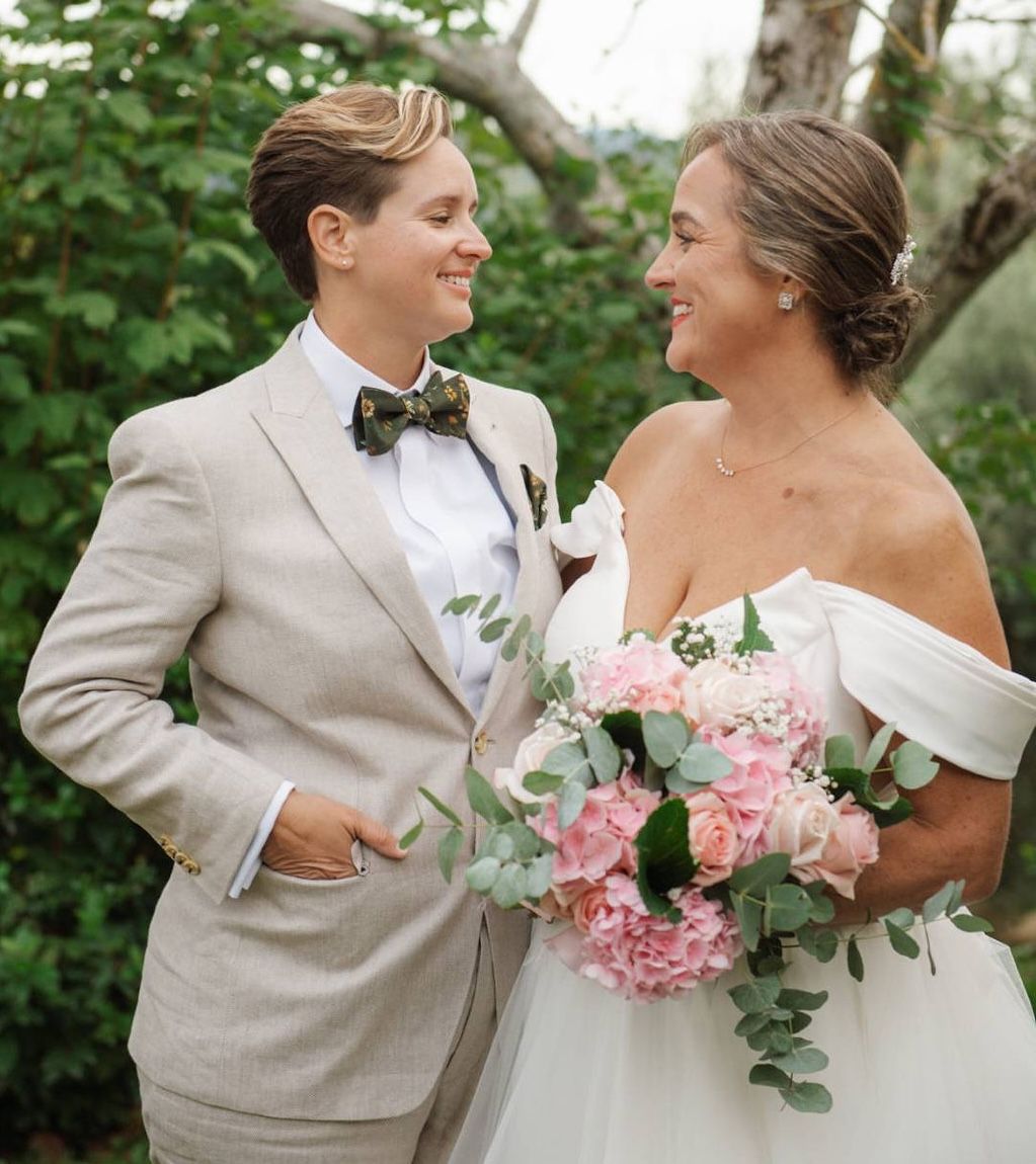 Newlyweds looking at each other with the bride holding a pink bouquet and with greenery in background