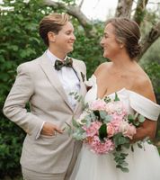 Newlyweds looking at each other with the bride holding a pink bouquet and with greenery in background