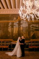 Bride and groom hugging with old paintings in the background and an exquisite chandelier during their vow renewal in Italy