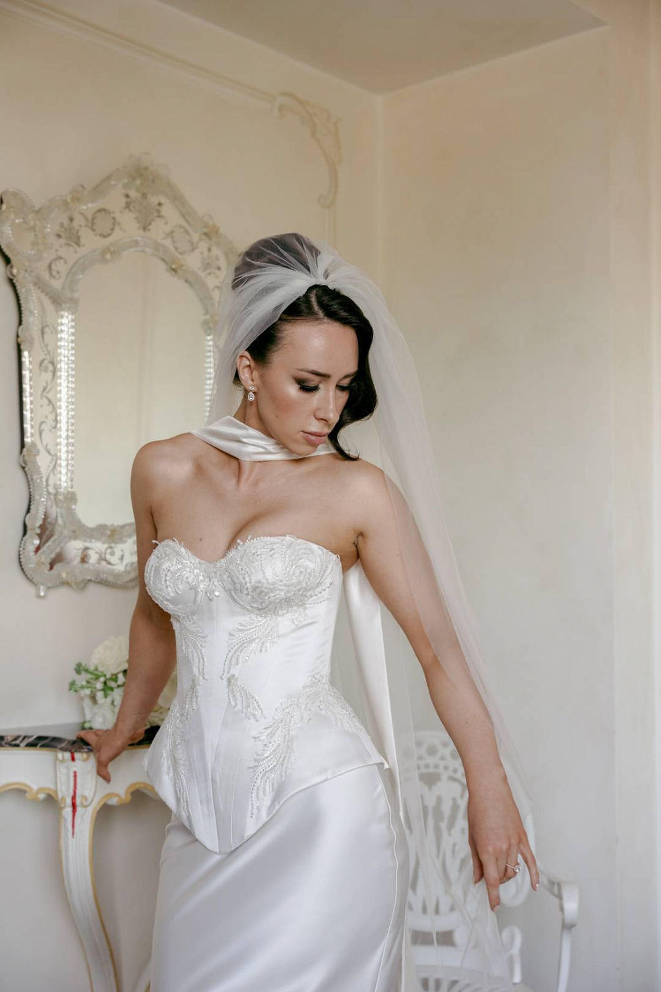 A bride wearing a modern white dress posing beside a mirror before her intimate wedding in Italy