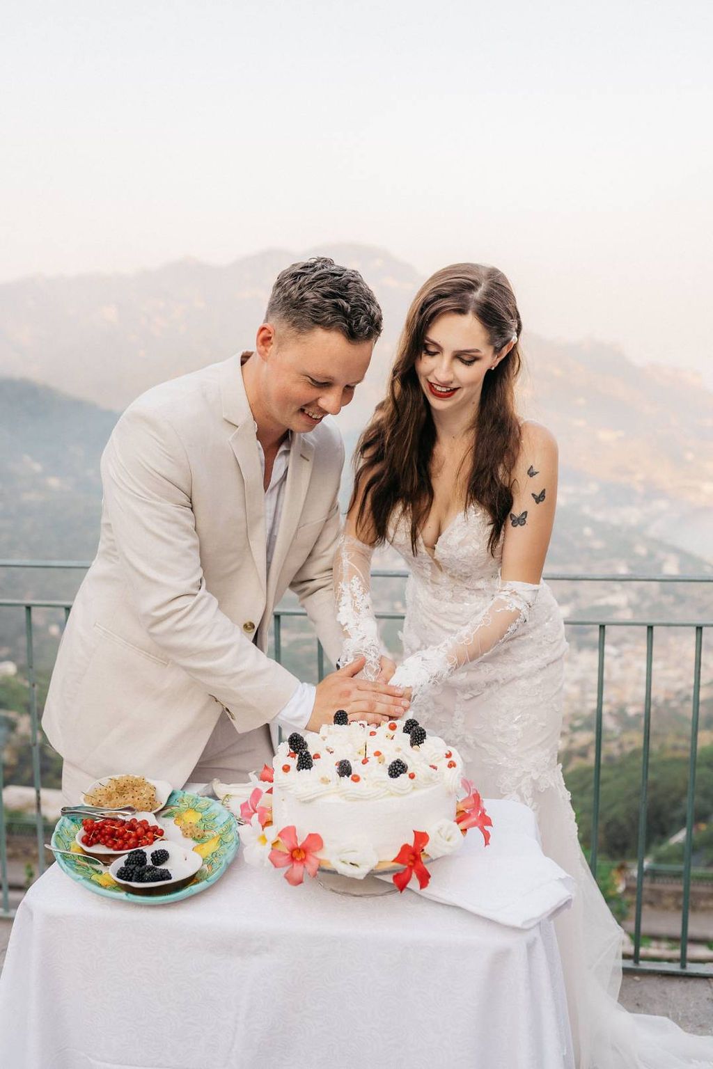 Bride and groom decorate their white wedding cake with icing and berries during the reception of their small wedding in Italy