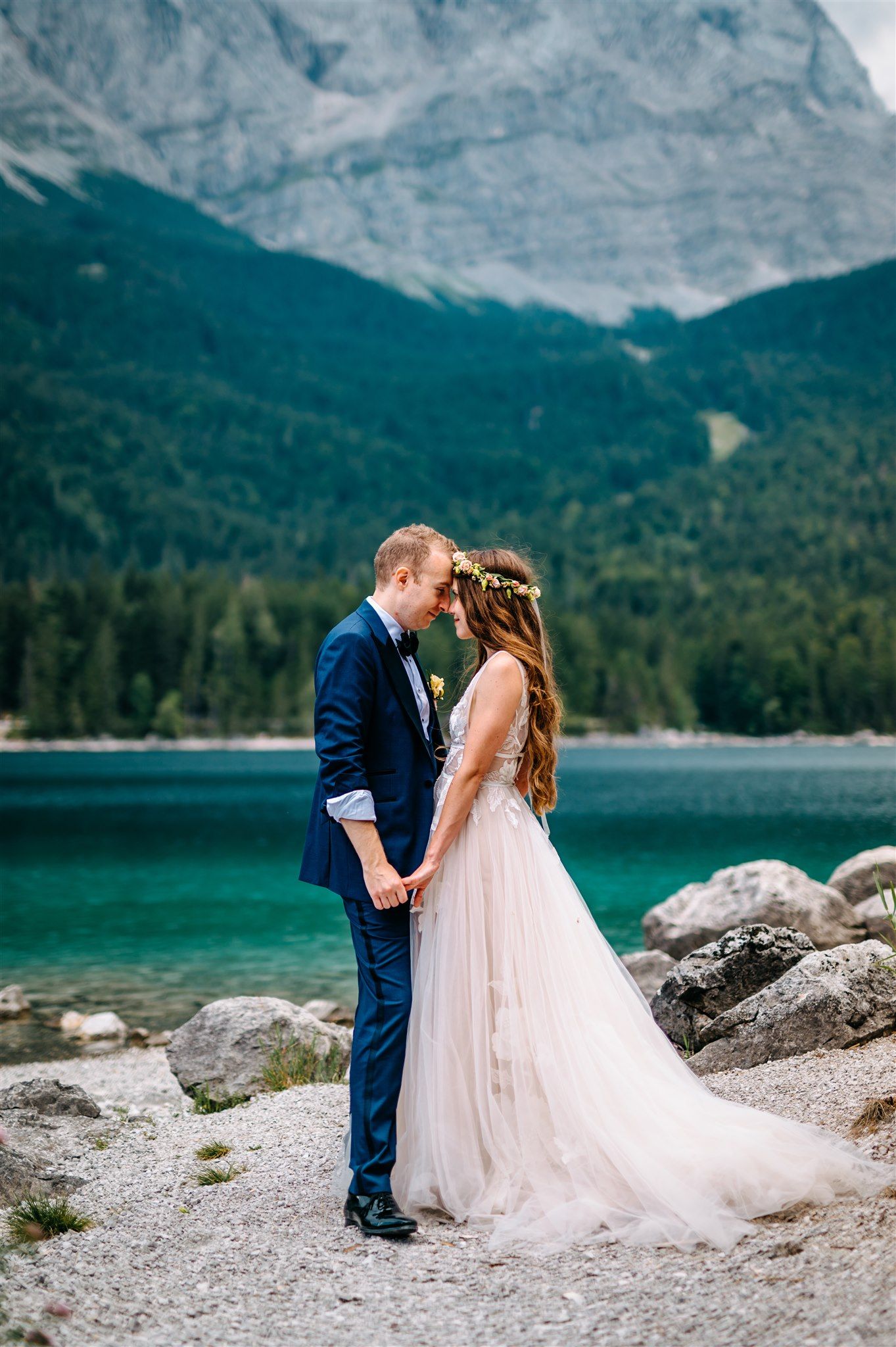 A bride and groom with their heads together beside a lake and the alpine mountains for their small wedding in Germany