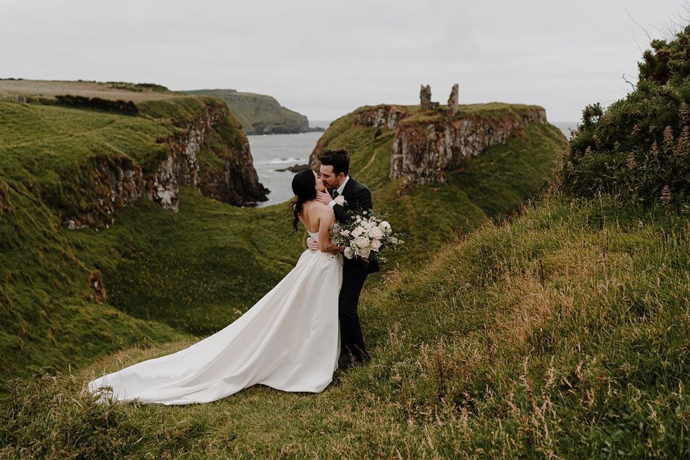 Bride holds a bouquet while kissing the groom above a mountain in Northern Ireland