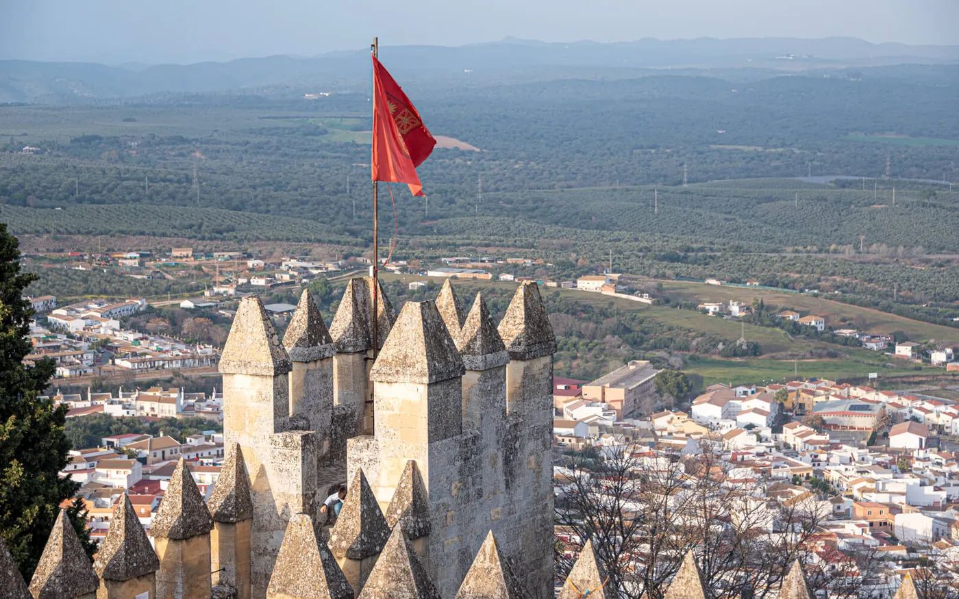 Andalusia’s landscape surrounded by greenery, with some medieval buildings, and a tall gothic castle with a red flag