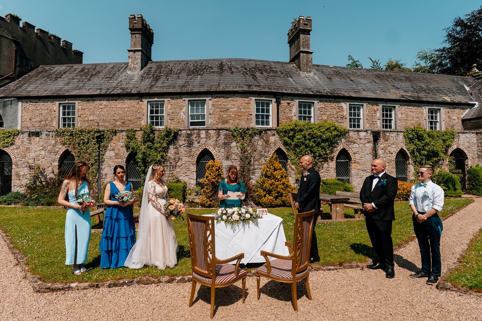 Bride and groom with their celebrant and entourage in a castle garden during the ceremony of their small wedding in Ireland