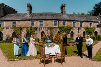 Bride and groom with their celebrant and entourage in a castle garden during the ceremony of their small wedding in Ireland