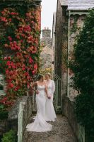 Newlyweds having a photoshoot during their autumn intimate wedding in Ireland with two rustic buildings covered in ivy plants in the background