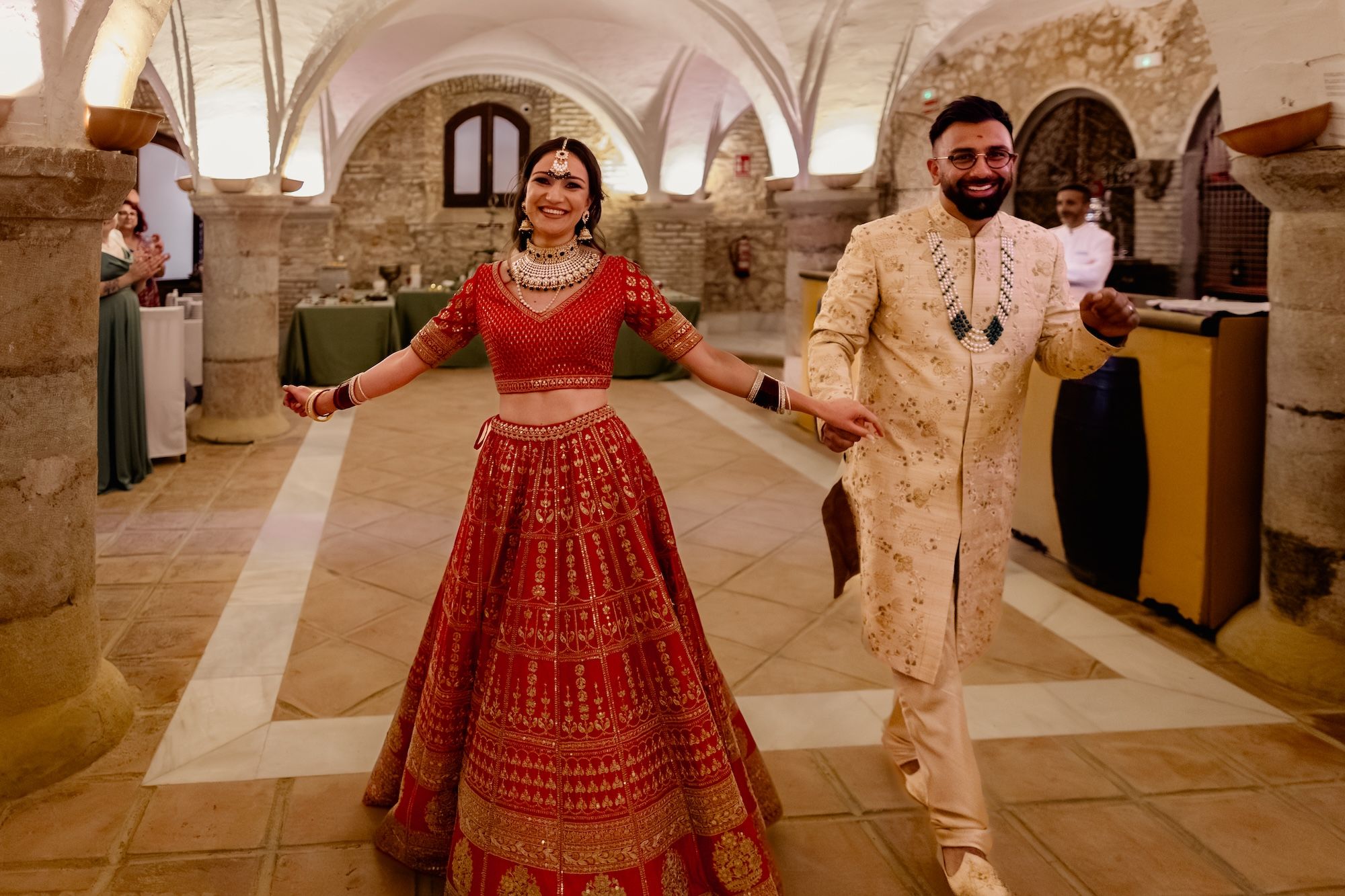 Newlyweds in Hindu wedding attire in celebratory mood, smiling as they walk inside a bodega during their destination wedding in Spain