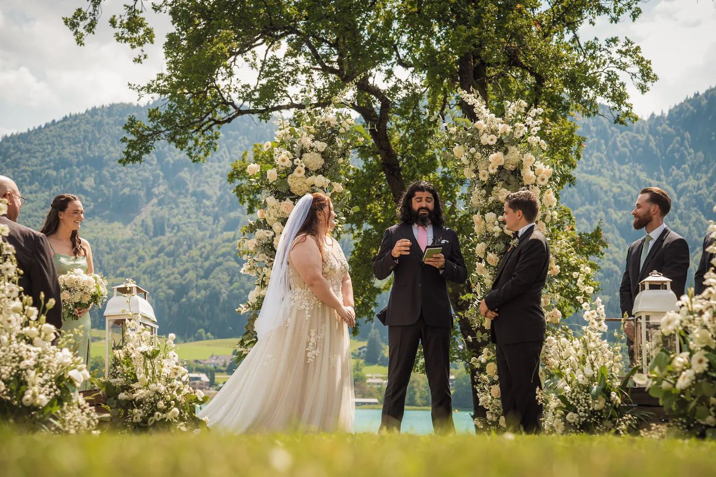 Couple saying their vows before a white floral arch at a mountain lake near Salzburg