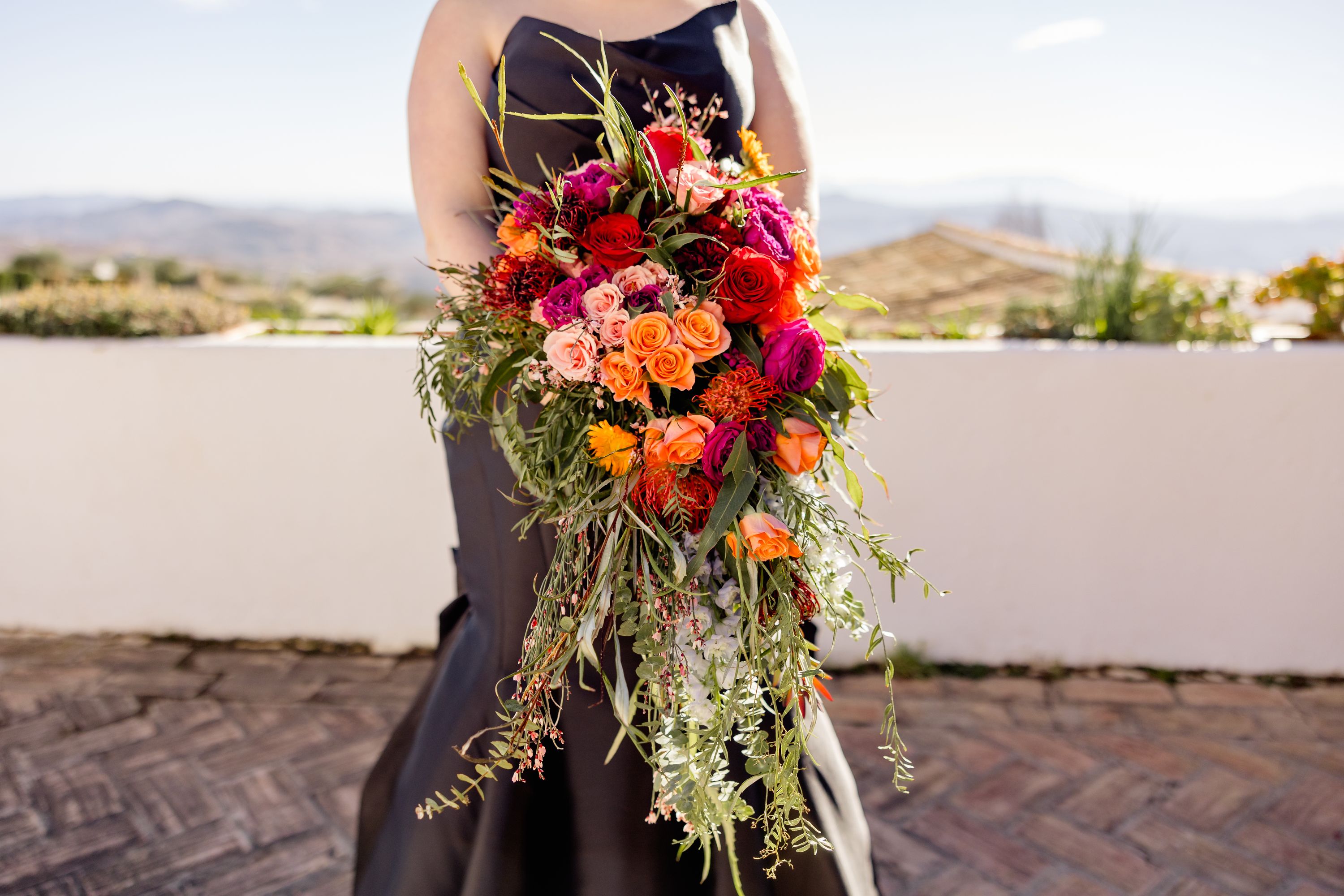 a colorful bouquet being held by a bride in black