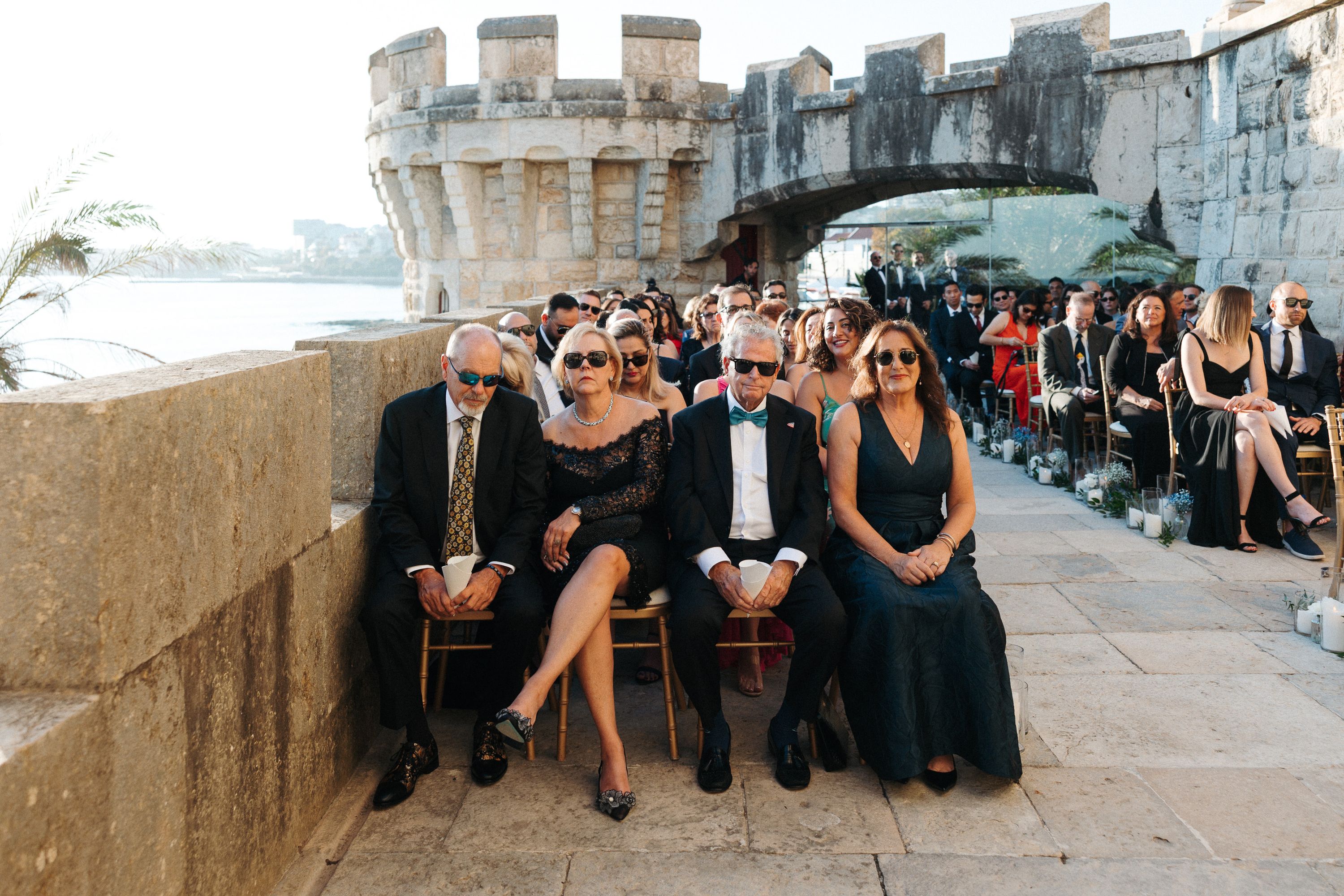Guests seated at a historic seaside fortress ceremony during a small wedding in Portugal with ocean views and stone architecture