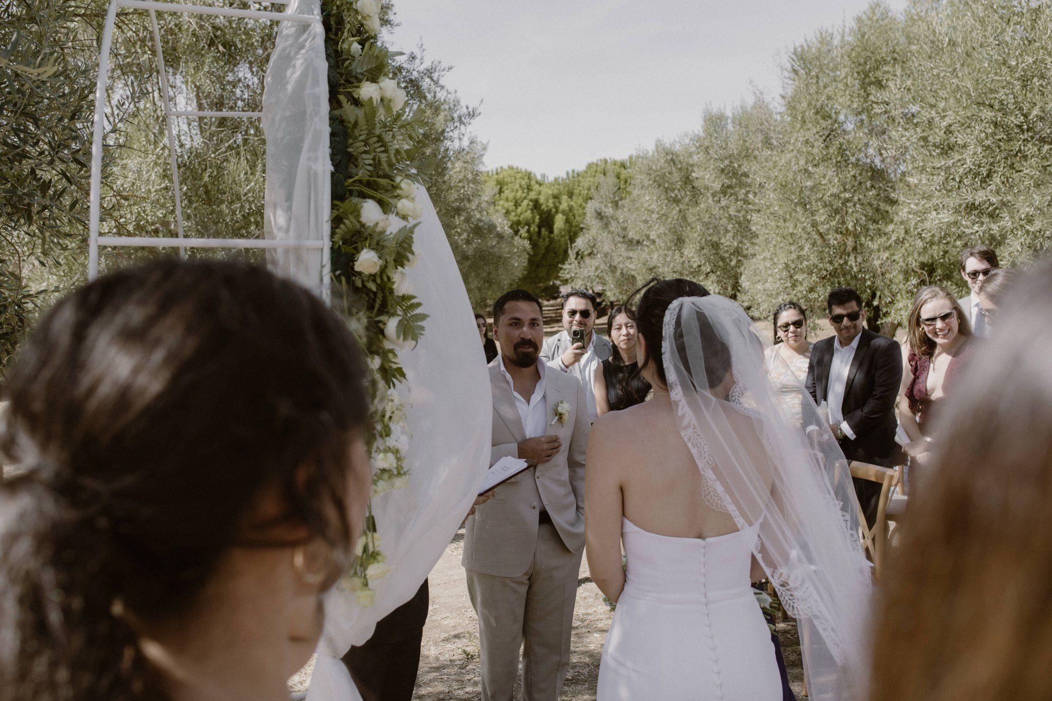 Groom looks at his bride with their guests in the background during an outdoor ceremony of an intimate wedding in Portugal