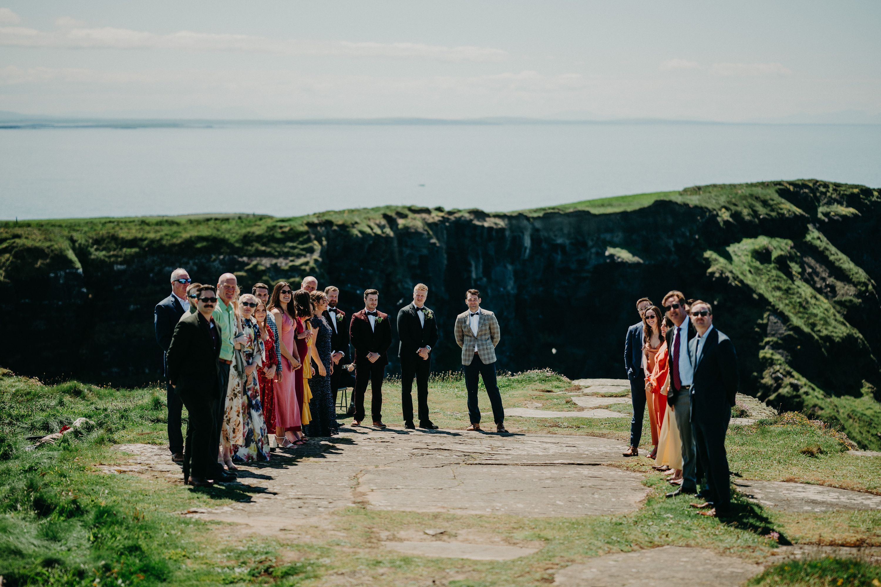 A groom with the entire party waiting for the bride on top of a cliff during their small wedding in Ireland