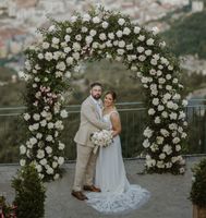 Newlyweds smiling at the camera during their destination elopement in Italy with a floral arch and Amalfi in the background