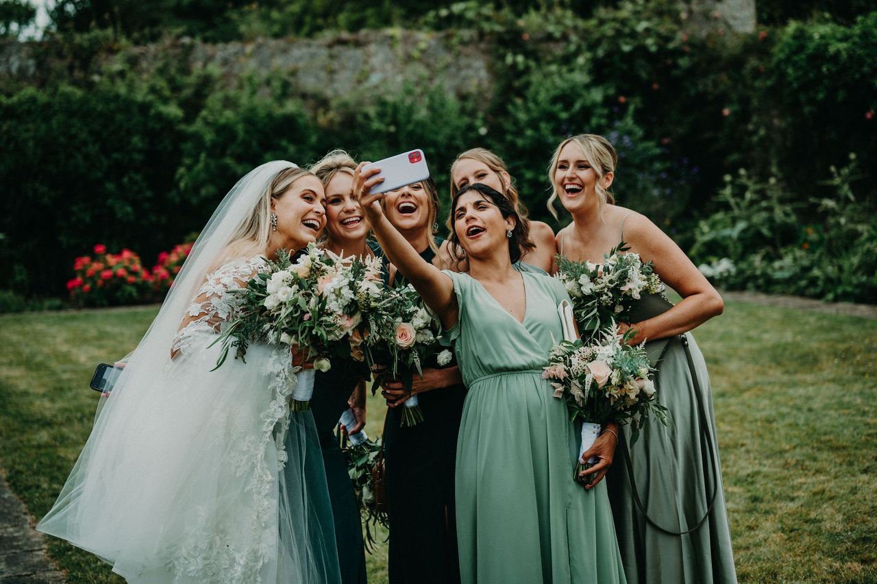 Bridesmaids in green with the bride in white holding their bouquets happily taking a selfie