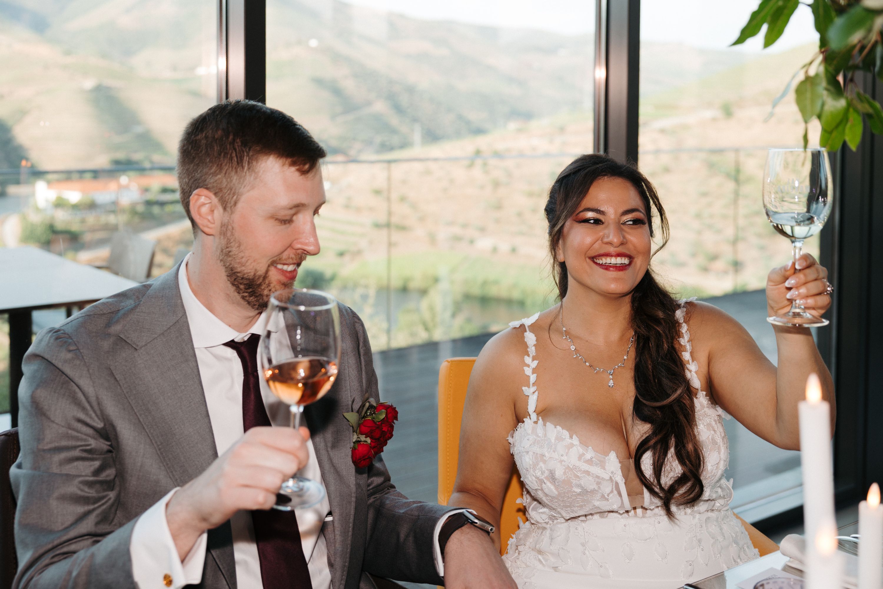 Newlyweds seated during their wedding reception in Portugal, holding glasses of wine with vineyards in the background