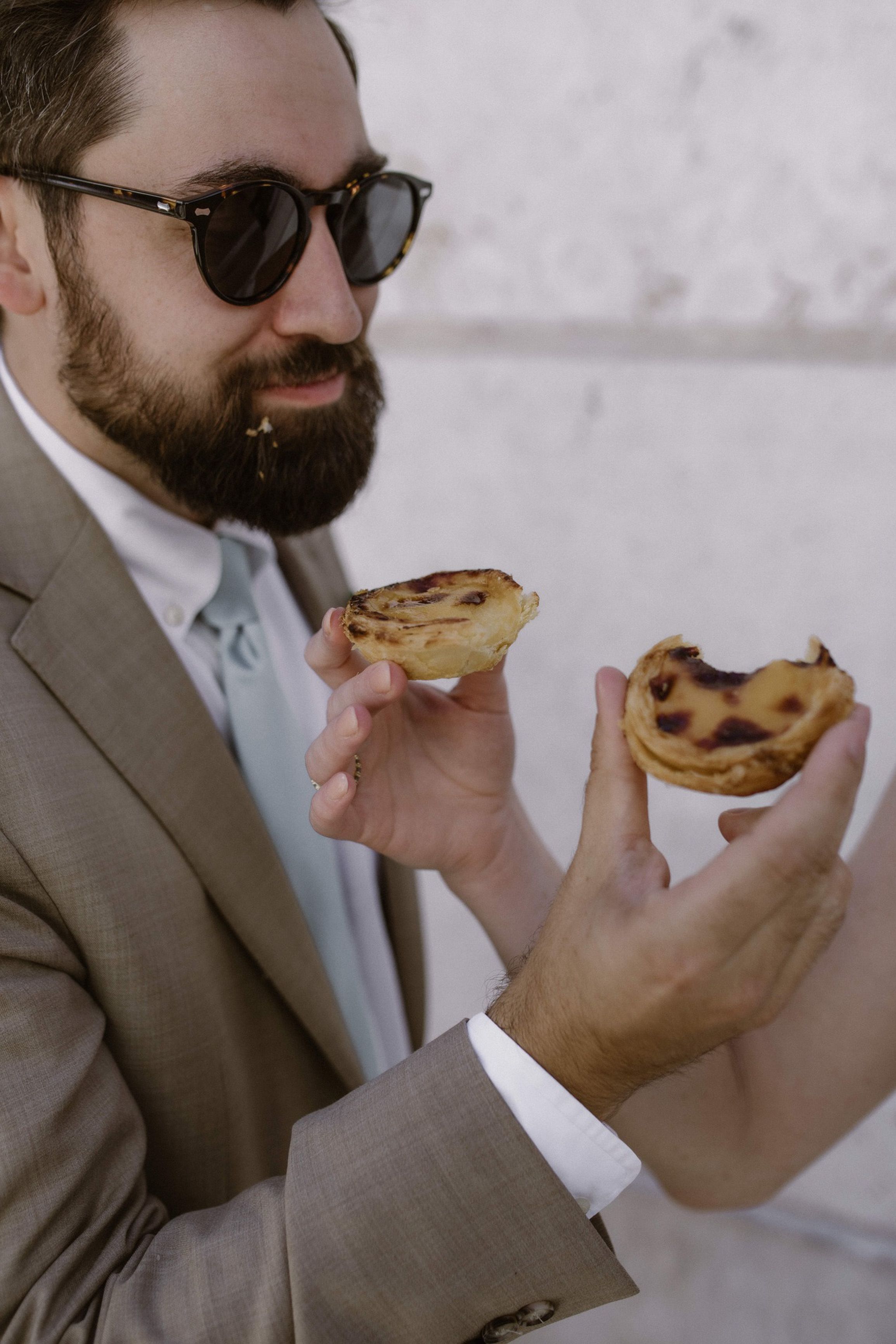 Newlyweds wearing sunglasses while tasting Portuguese pastries at an intimate wedding in Portugal