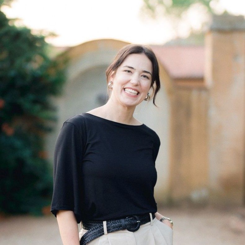 Wedding planner in Italy standing and smiling in front of the camera with a medieval stone wall in the background.