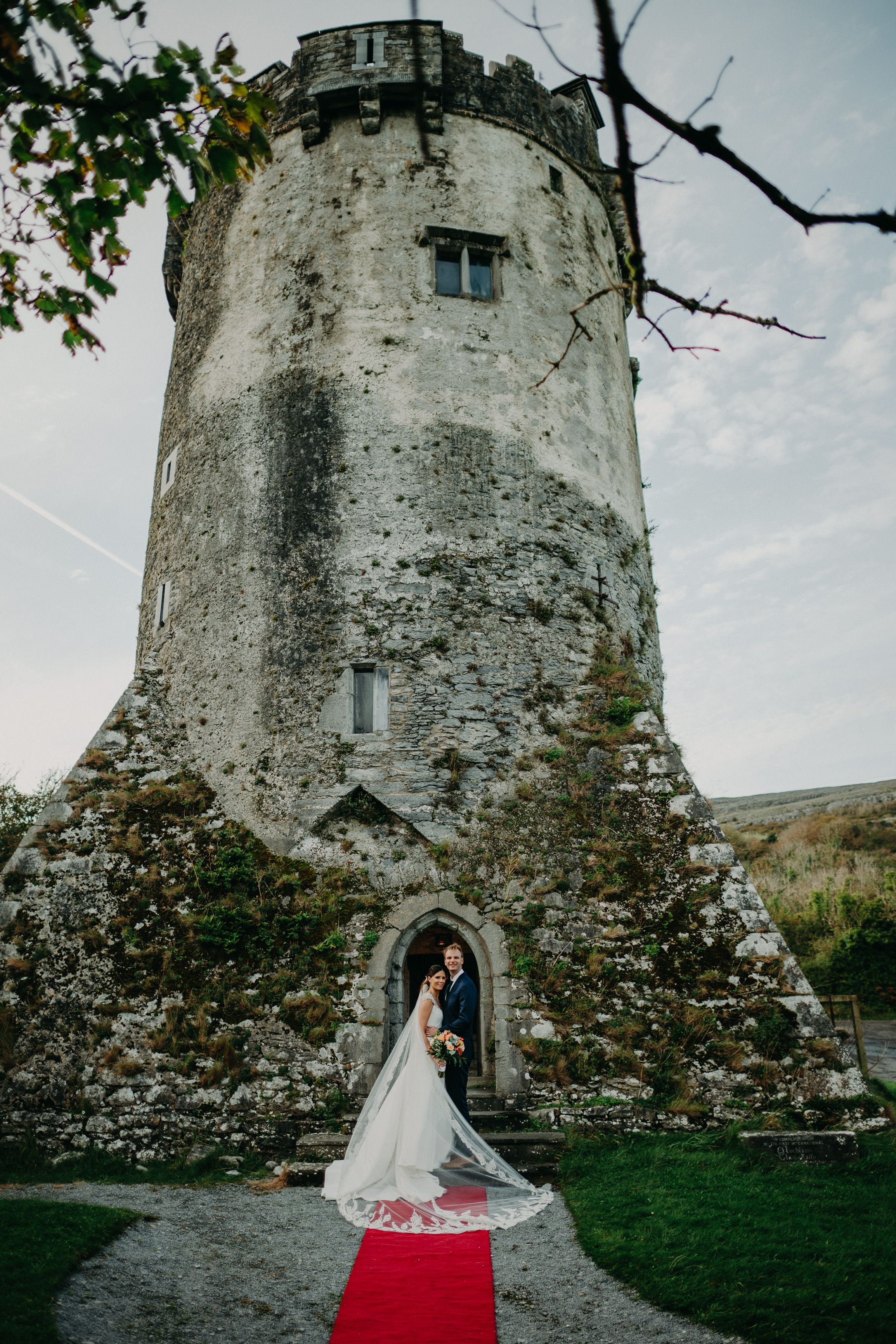 Bride and groom posing beneath a medieval tower during an intimate wedding in Ireland with a dramatic castle backdrop.