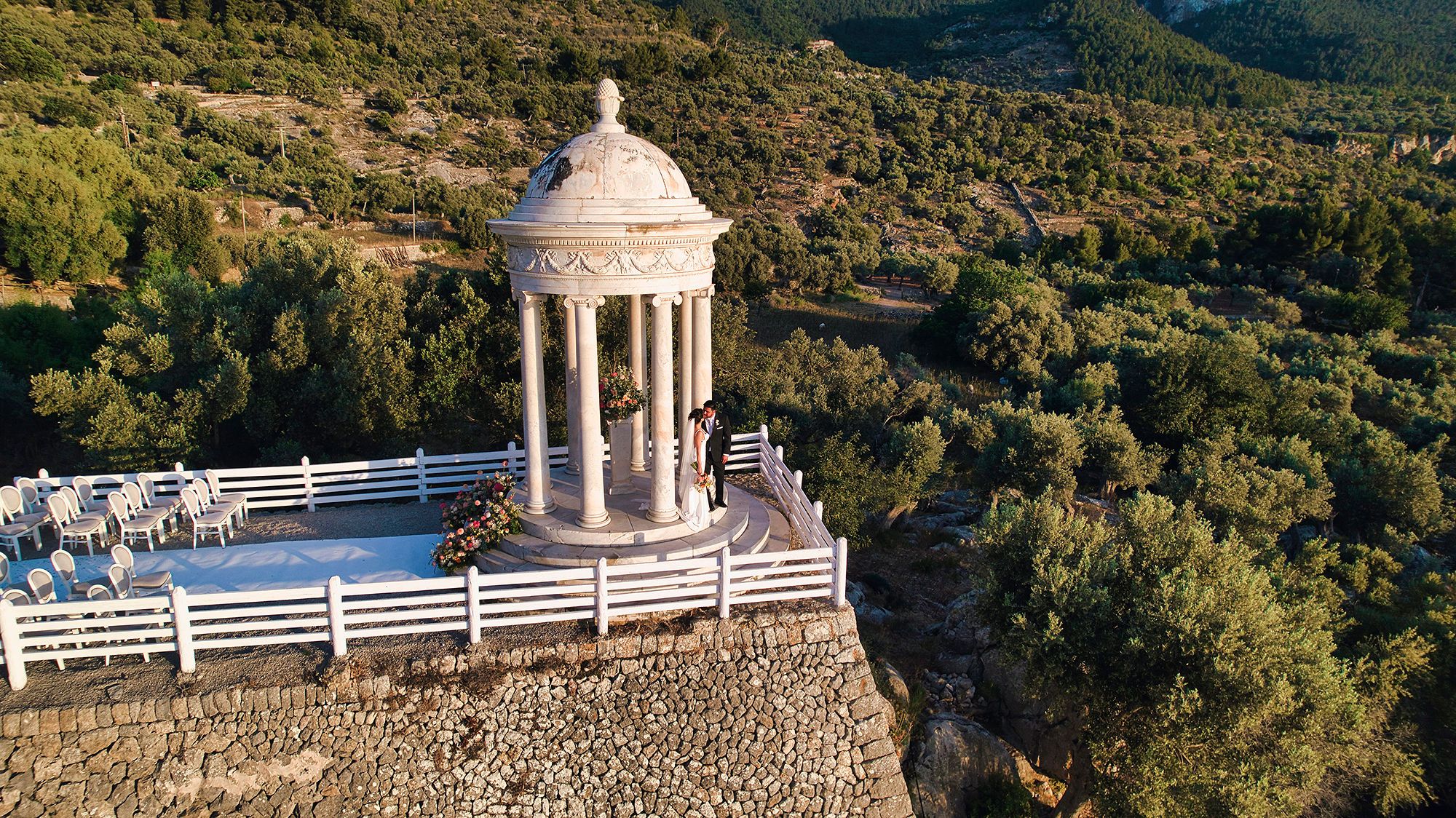 A scenic photo of the newlyweds kissing inside a marble temple in a clifftop venue in Mallorca during their small wedding in Spain