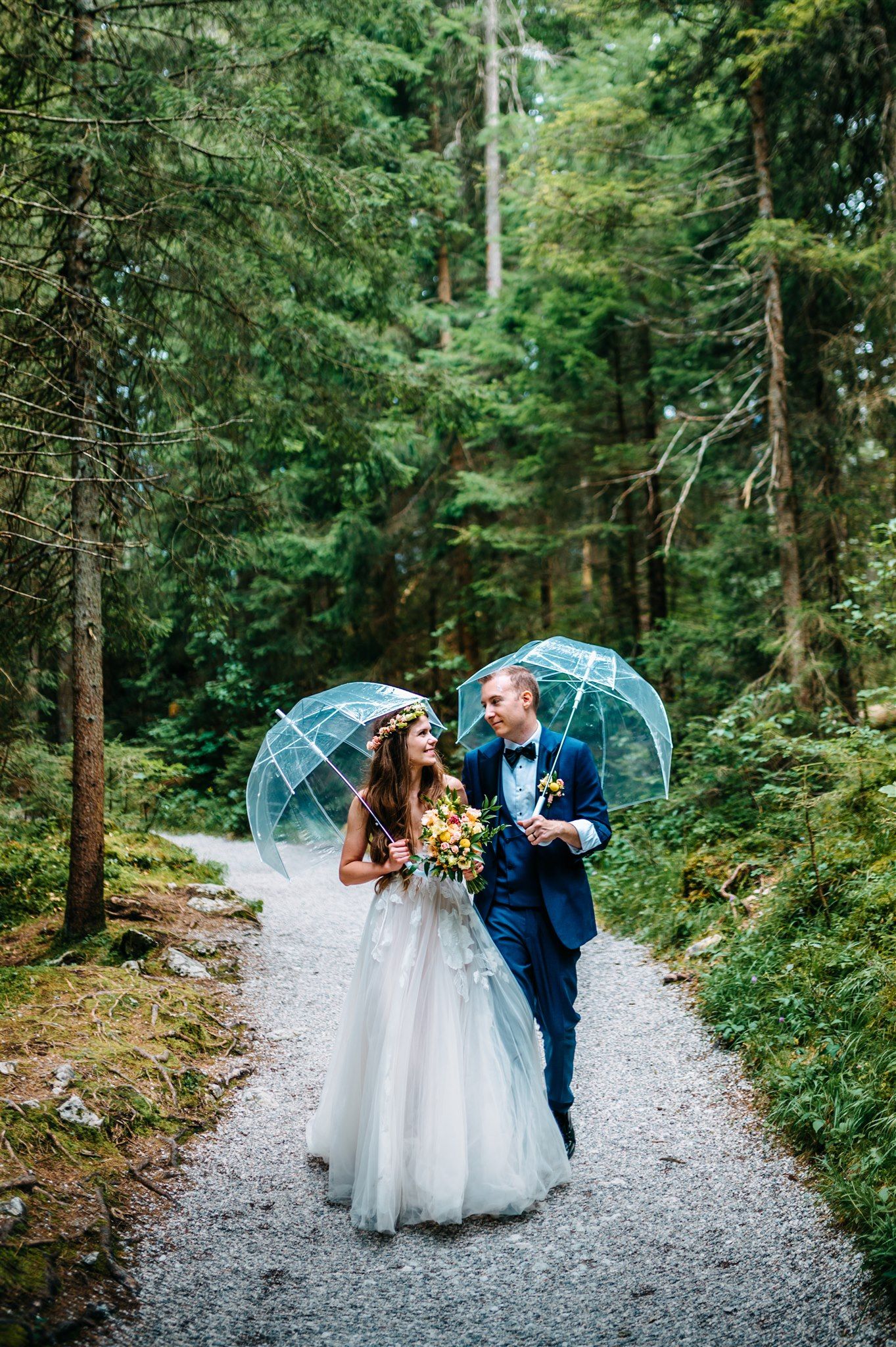 A bride and groom holding umbrellas while walking through a forest during their intimate wedding in Germany