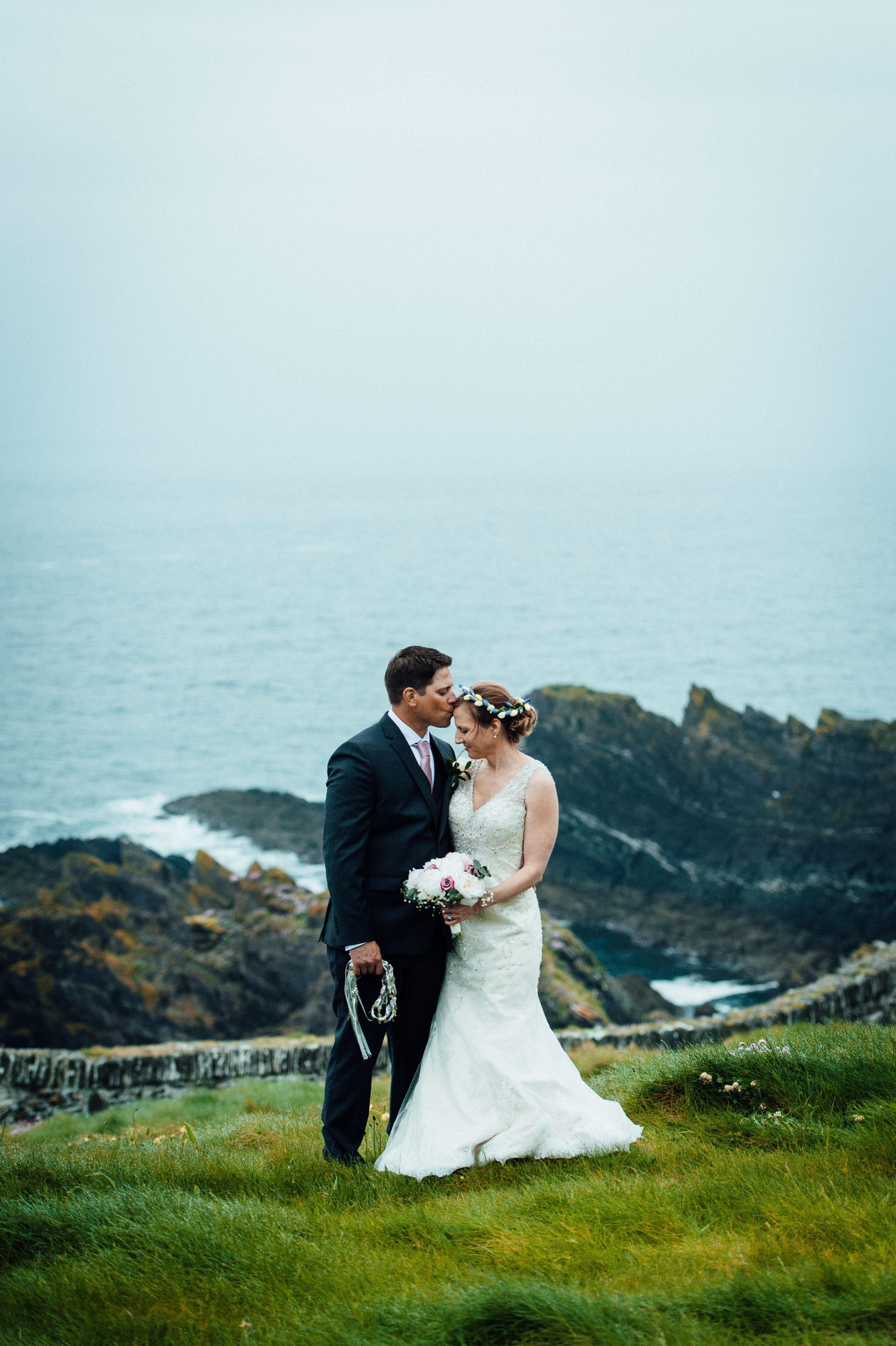 Groom kisses bride’s forehead after the ceremony of their destination wedding in Ireland atop a cliff in County Cork