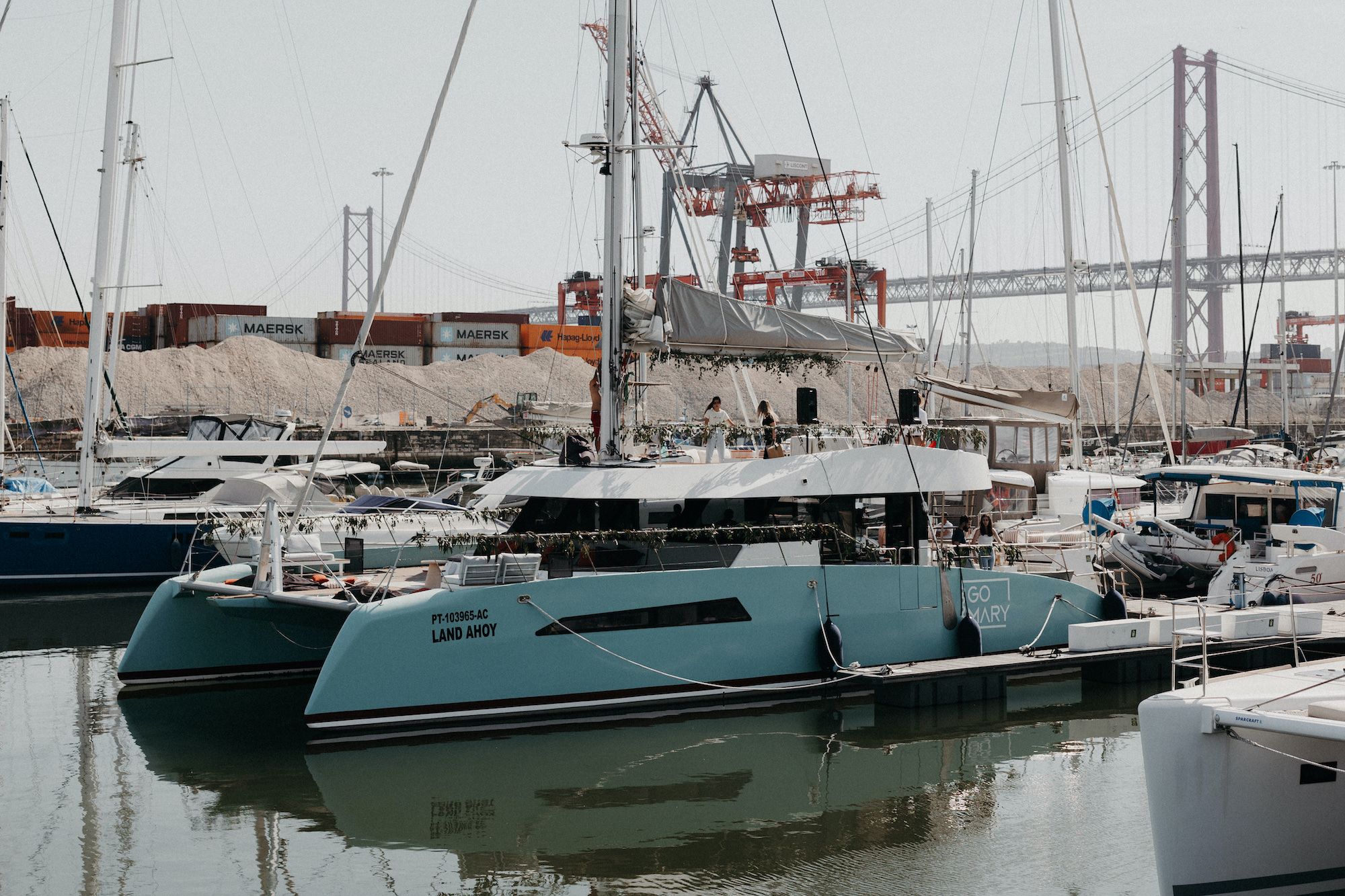 A blue sailboat along a port in Tagus River with people inside decorating for a destination wedding in Portugal