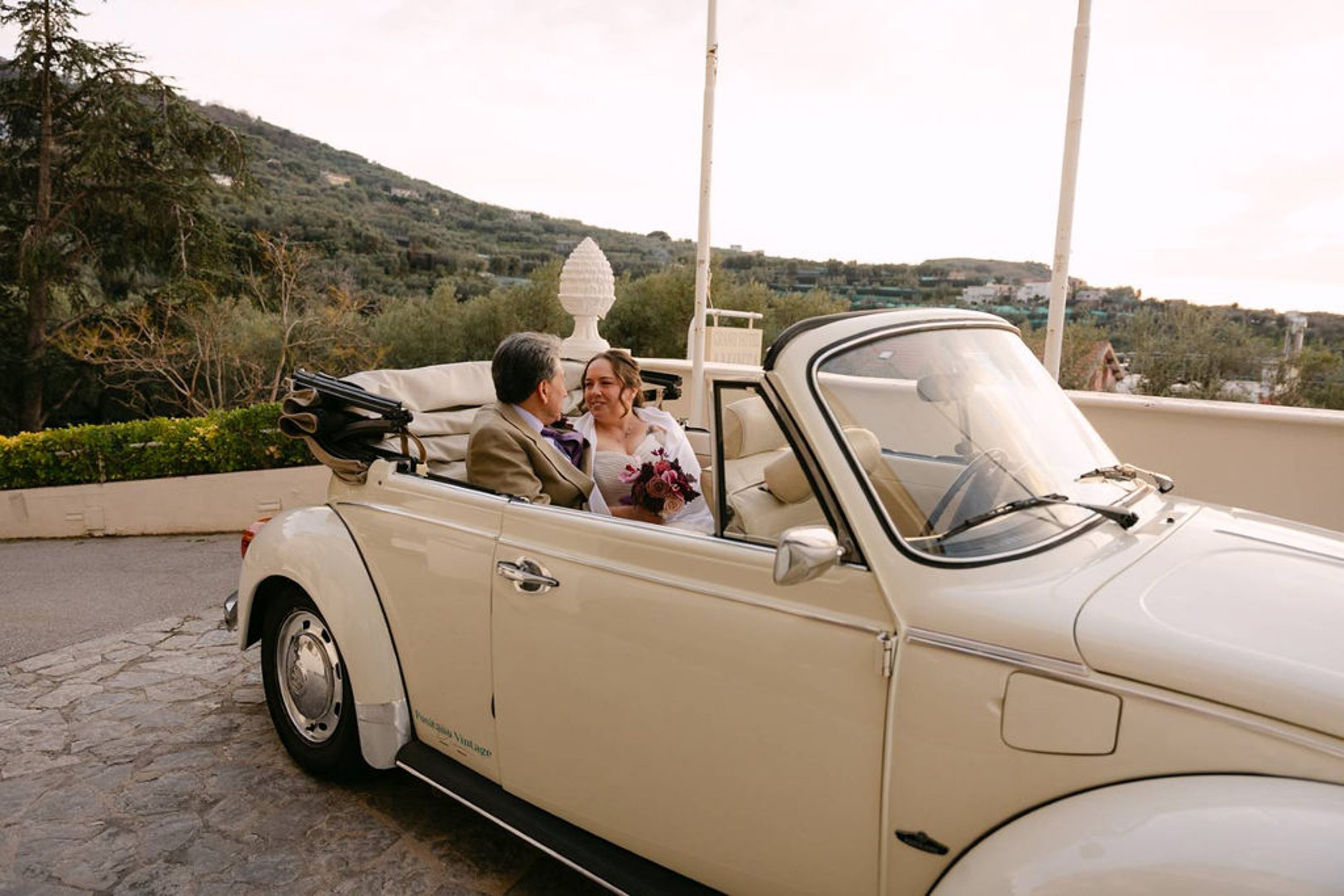 Bride and groom ride in a vintage convertible during an intimate wedding in Italy