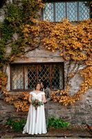 Bride and groom posing in front of a cottage with crawling ivy in autumn blooms during their elopement in Ireland