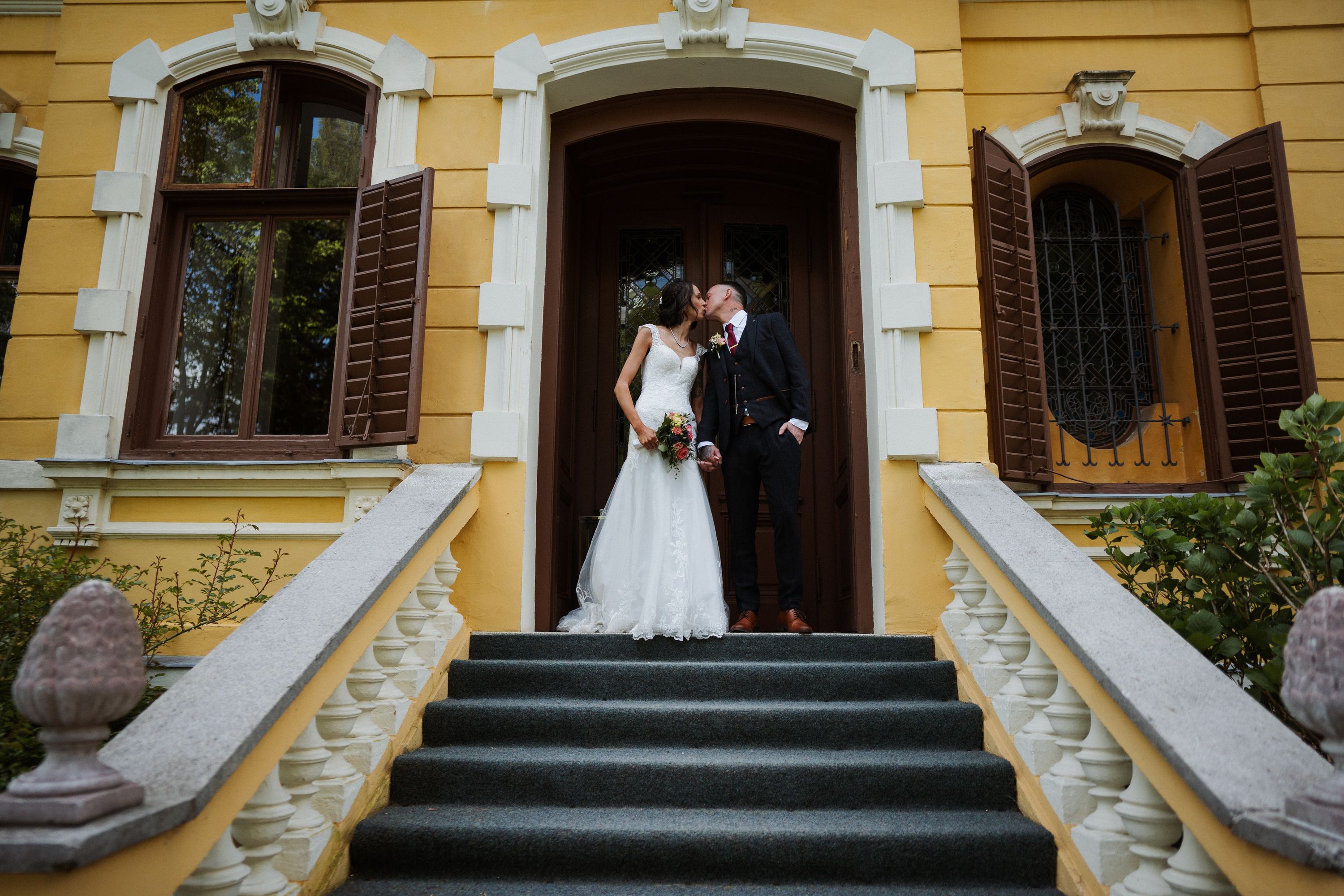 Newlyweds kissing on the steps of a historic yellow villa in Austria