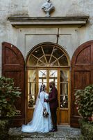 Groom holds his bride on her waist facing each other in front of a glass & wooden wall of a villa where they eloped in Italy