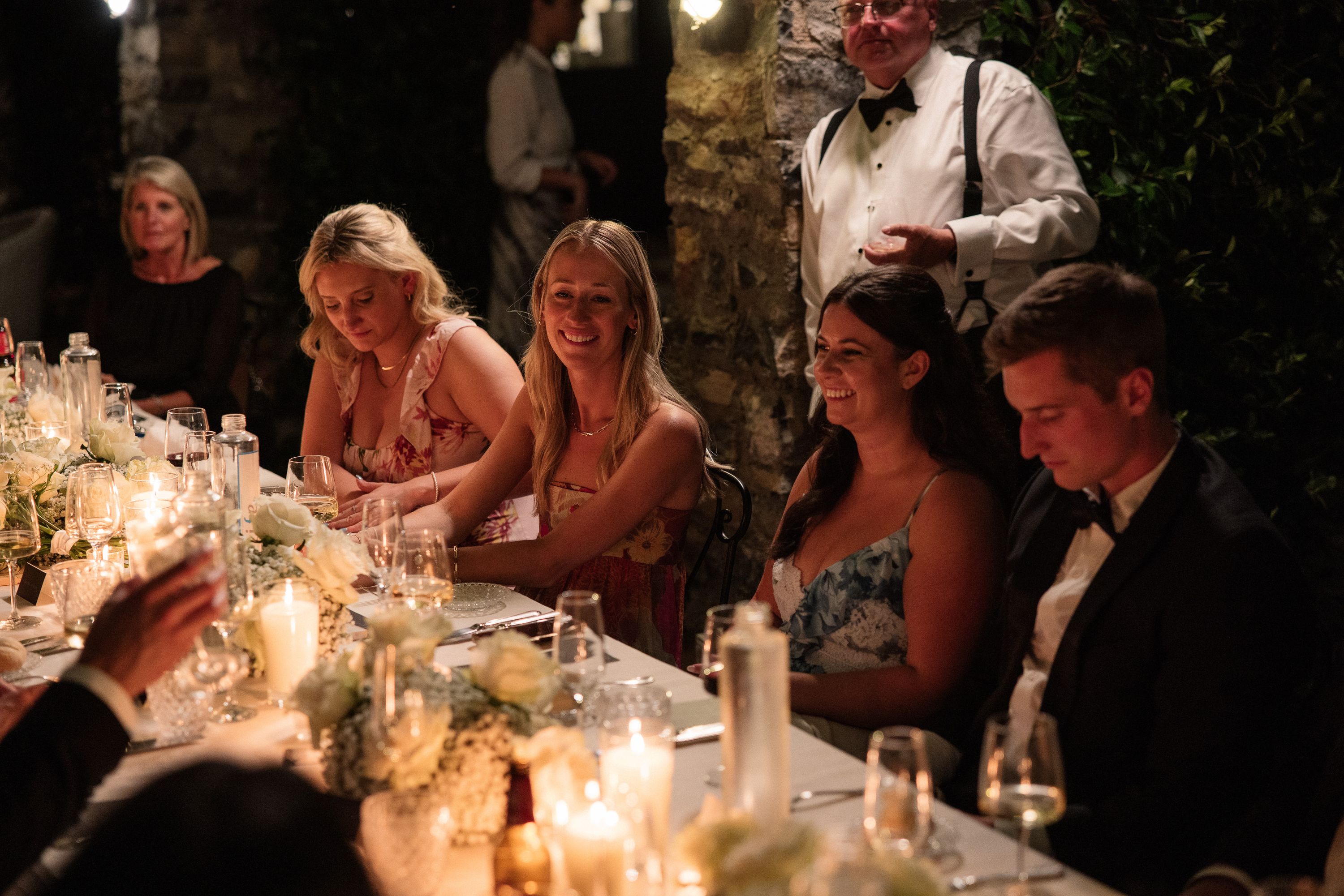 Wedding guests gather around a candlelit dinner table at an intimate wedding in Italy evening celebration