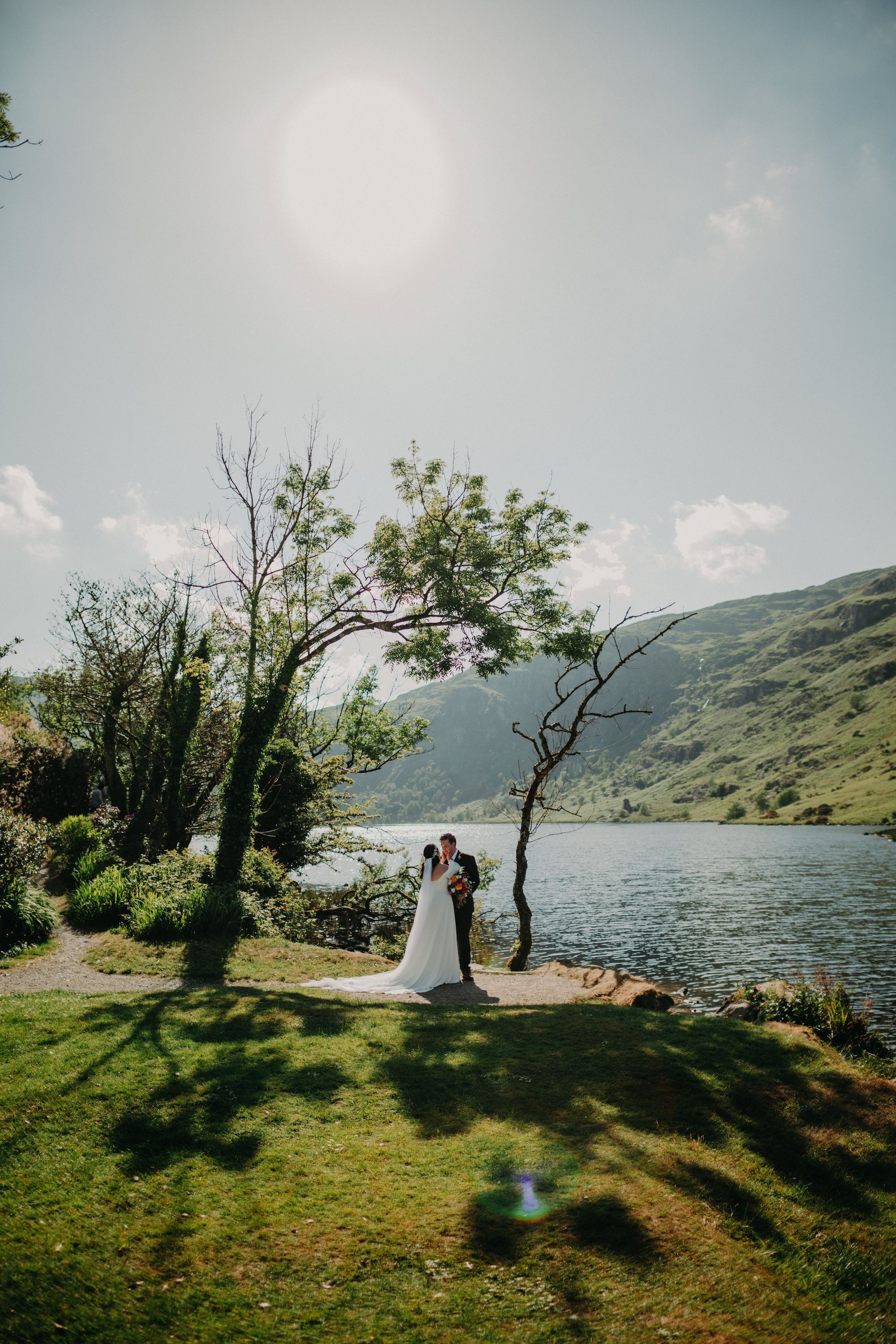 Bride and groom having a photoshoot outdoors with the Irish lake, trees, and mountains in the background