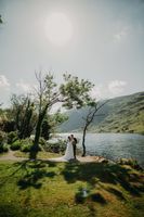 Bride and groom having a photoshoot outdoors with the Irish lake, trees, and mountains in the background