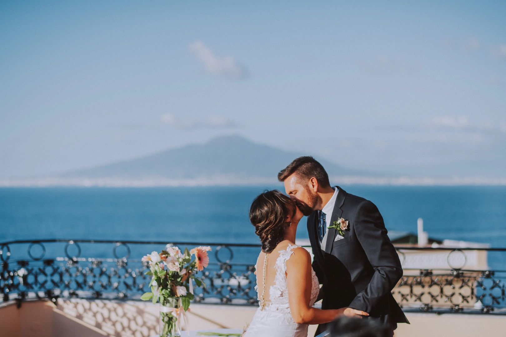 Bride and groom kissing on a terrace with ocean views and volcano in the background