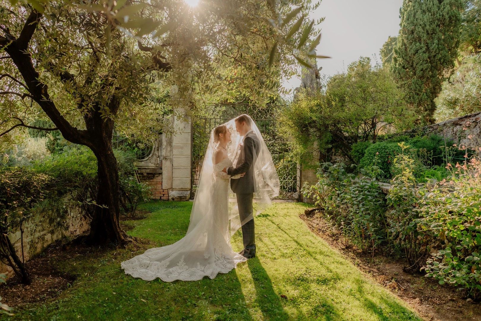 Bride and groom looking at each other under the veil in the middle of a garden of the venue where they got married in Italy