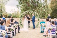 Couple with a floral arch background hold hands during an outdoor wedding ceremony in France.